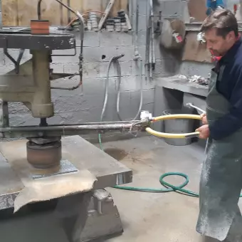 Marbrier en tablier guidant une machine de taille sur un plan de pierre, dans son atelier
