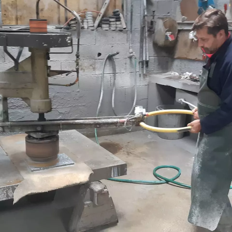 Marbrier en tablier guidant une machine de taille sur un plan de pierre, dans son atelier