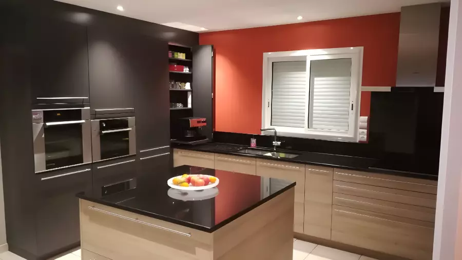 Îlot central et plan de travail en granit noir poli dans une cuisine en bois clair à mur rouge