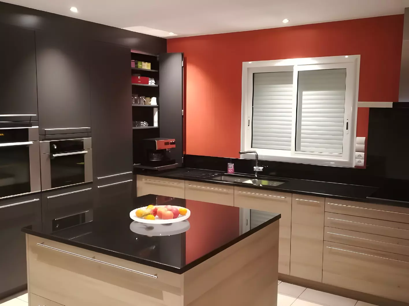 Îlot central et plan de travail en granit noir poli dans une cuisine en bois clair à mur rouge