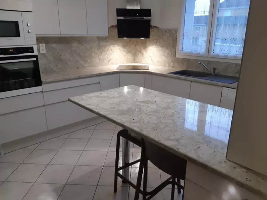 Table de cuisine et crédence en granit clair veiné dans une cuisine blanche en L