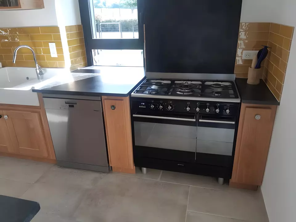 Plan de travail en pierre noire mate encadrant un piano de cuisson, avec évier en céramique