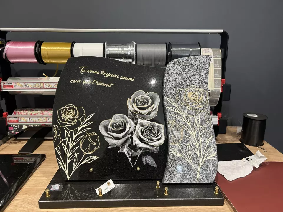 Deux plaques de granit gravées de roses et d'un bouquet, posées à l'atelier devant la machine de gravure