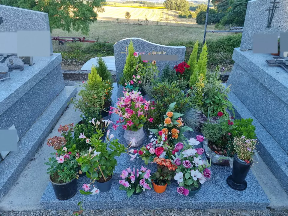 Monument funéraire en granit gris, stèle galbée à croix dorée, tombale entièrement fleurie