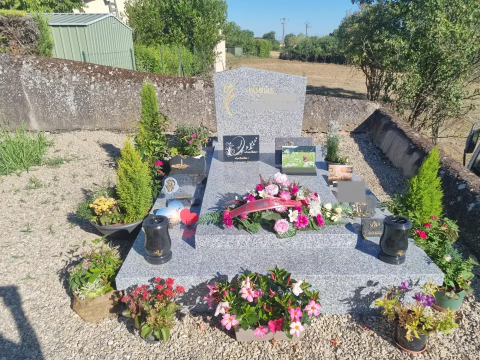 Monument funéraire en granit gris clair, stèle ornée d'épis dorés, tombale garnie de fleurs et de plaques