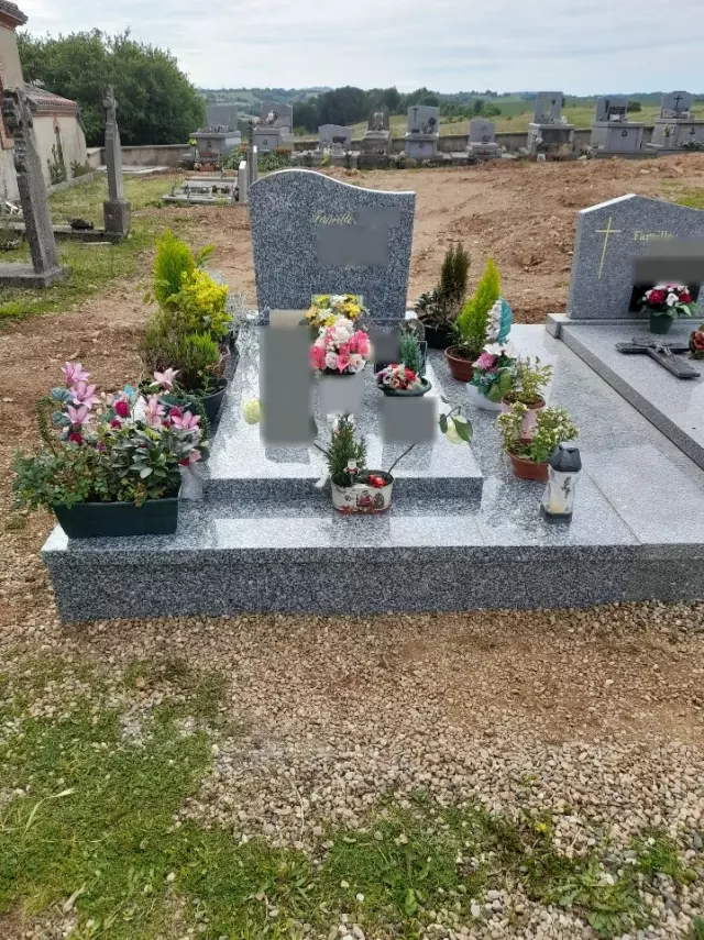 Monument funéraire en granit gris, stèle galbée, tombale garnie de fleurs et de plaques