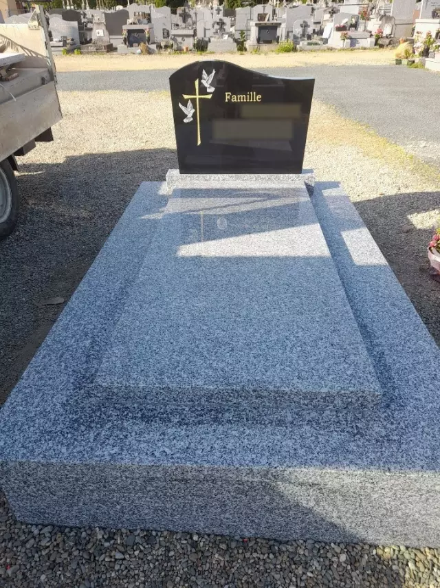 Stèle en granit noir ornée de deux colombes et d'une croix dorée, sur une tombale en granit gris clair